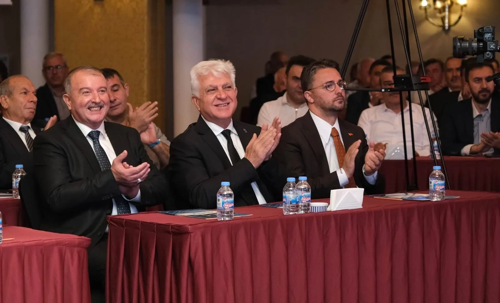 Ankara’daki mobilya toplantısında üç yönetici, salondaki katılımcılarla birlikte alkışlıyor.
