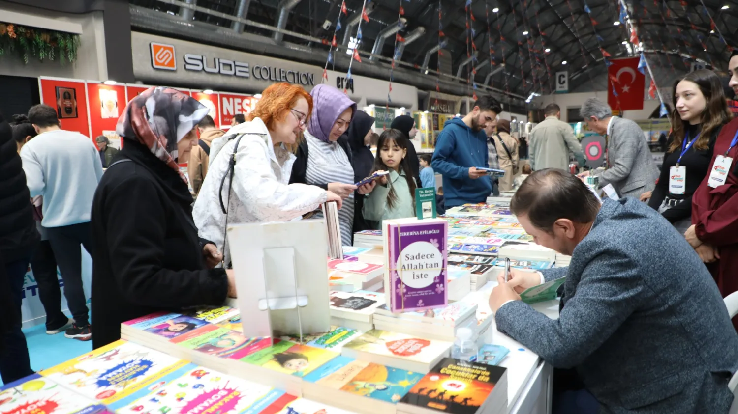 İnegöl Kitap Günleri’nde okuyucular kitapları incelerken bir yazar masada kitap imzalıyor.