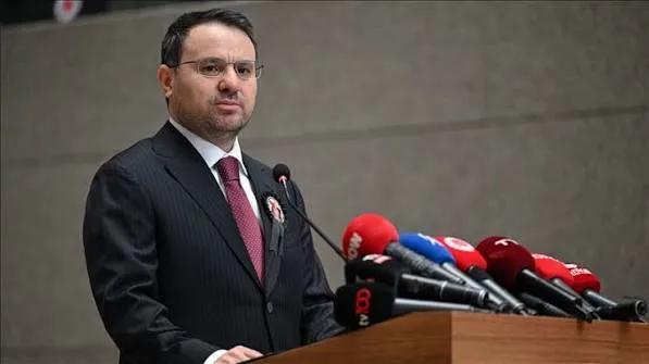 Takım elbiseli bir yetkili, çok sayıda mikrofonun önünde kürsüde açıklama yapıyor