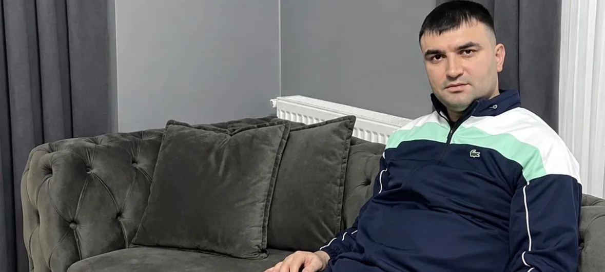 Mekin Büyükdeniz, gri bir koltukta otururken kameraya bakıyor.